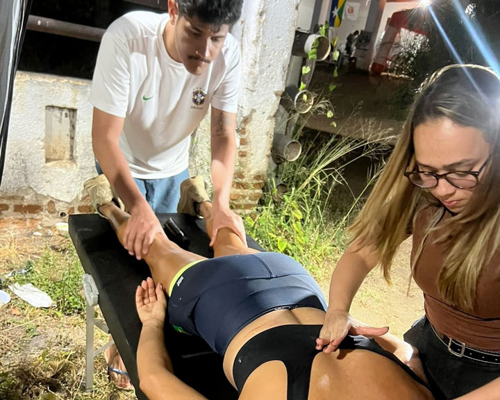 À noite, Lua está deitada em uma maca enquanto um homem cuida de suas pernas e uma mulher toca seu ombro.